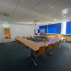Großer Seminarraum mit Tischen und Stühlen für eine Konferenz oder Schulung und Notausgang.